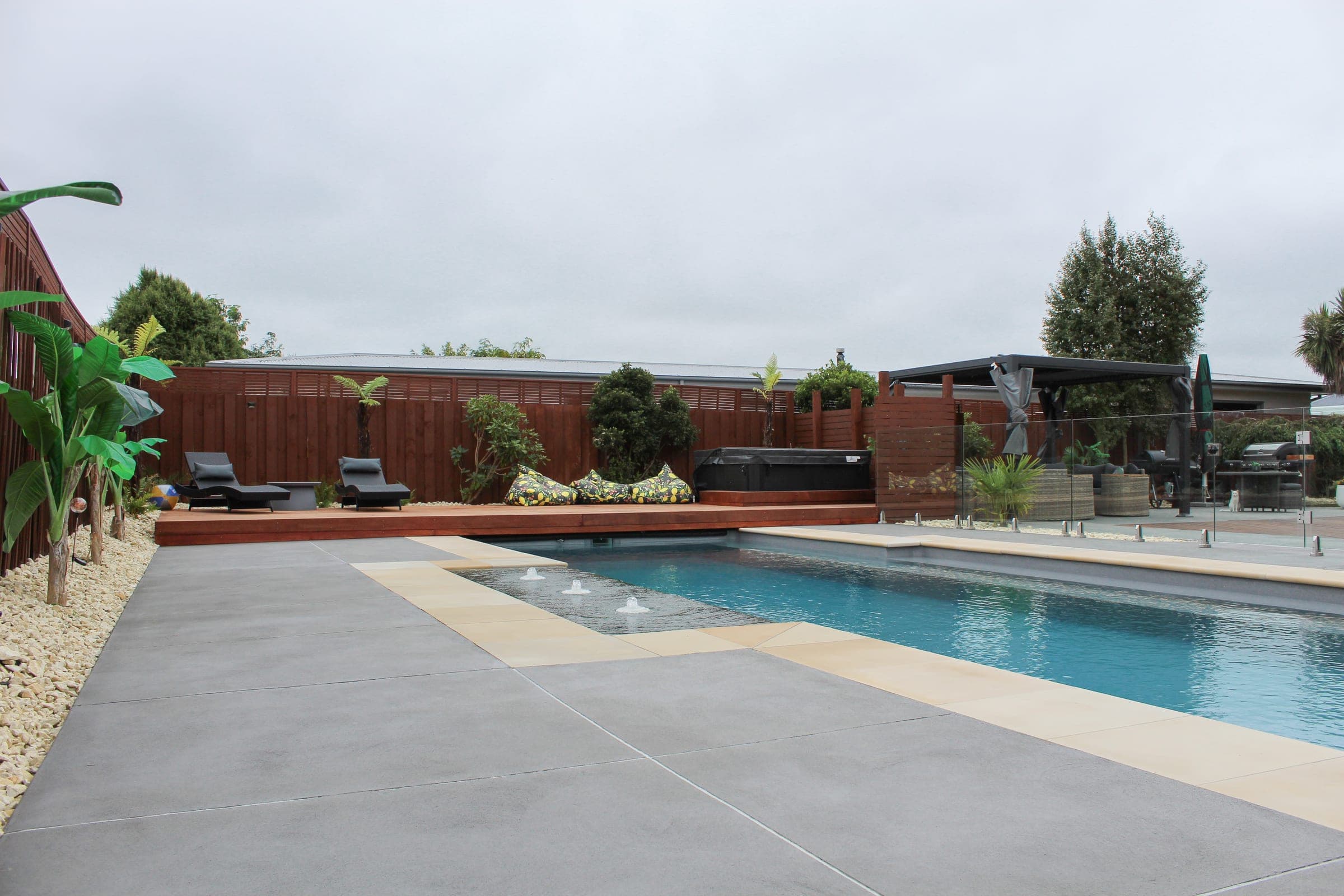 Honed sandstone coping and glass fencing framing the existing pool against large-format concrete.