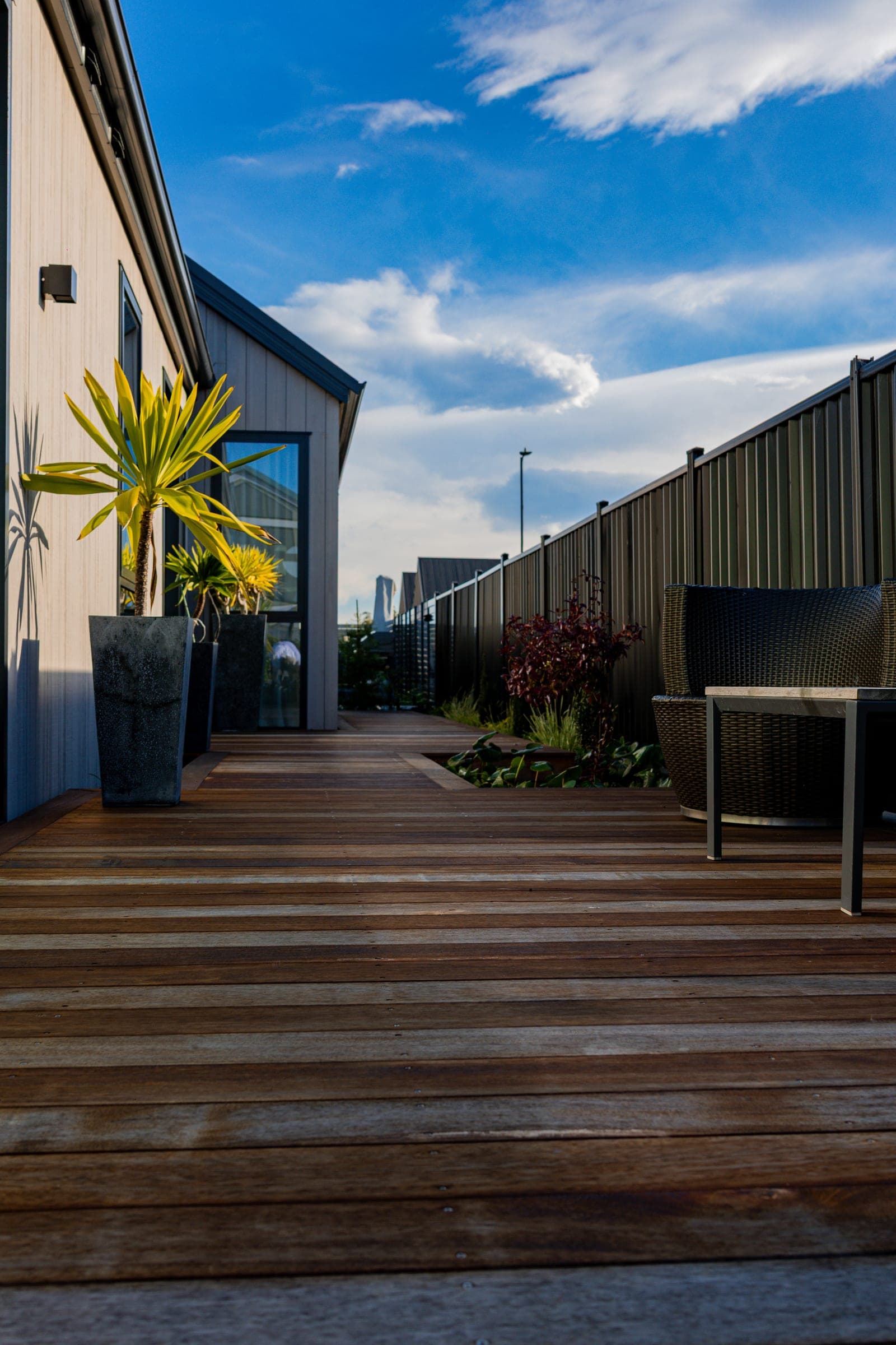 Warm hardwood decking running alongside the house, framed by dark slat fencing.